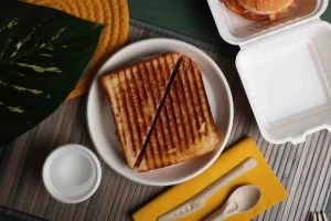 A beautifully arranged eco friendly disposable plate set made of sugarcane and palm leaf on a rustic wooden table, surrounded by fresh food and green leaves.