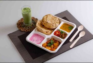 A beautifully set table with eco-friendly disposable plates with compartments, filled with neatly separated food items at an outdoor event or catering setup.