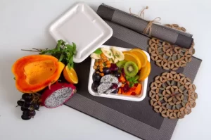 A close-up of biodegradable sugarcane-based packaging products like plates, trays, and bowls displayed on a natural jute tablecloth with branding tags from Indian eco brands.